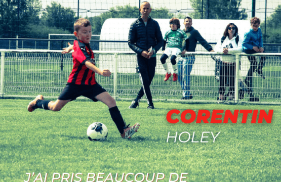 Corentin Holey en action sur le terrain de football, prêt à tirer, sous le regard de son entraîneur et de spectateurs