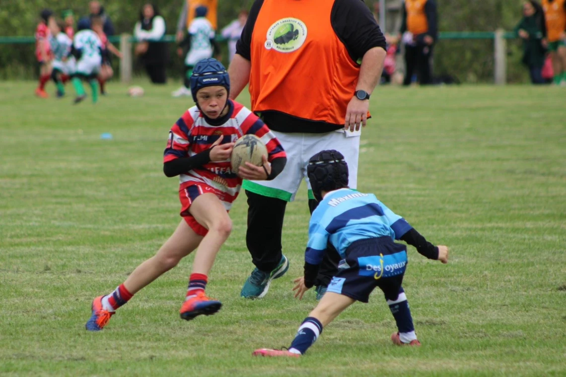 Des enfants jouant au rugby sur un terrain, l'un d'eux s'apprête à passer un adversaire avec le ballon en main