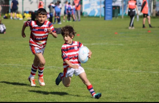 Des enfants jouant au rugby sur un terrain, l'un d'eux s'apprête à passer un adversaire avec le ballon en main